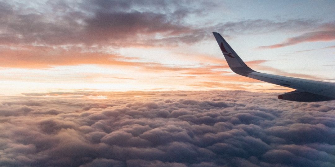 Airplane flying above clouds with sunset in background