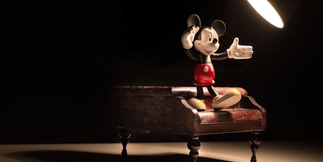 Toy Mickey Mouse standing on a piano underneath a light