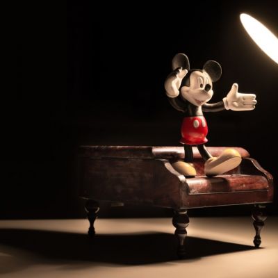 Toy Mickey Mouse standing on a piano underneath a light