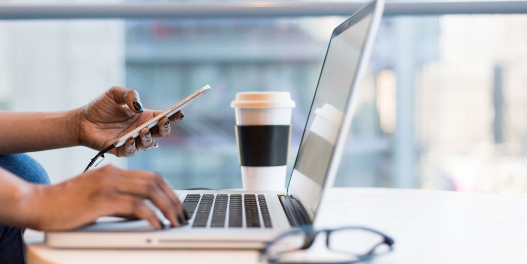 Remote worker with cell phone in one hand and other hand on laptop