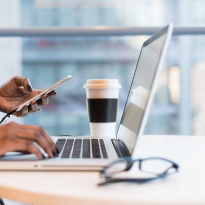 Remote worker with cell phone in one hand and other hand on laptop