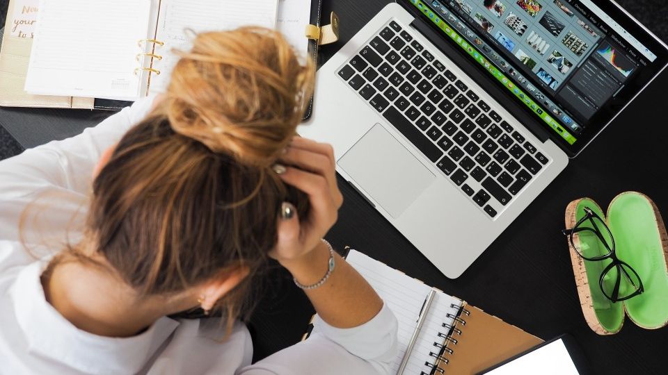 A stressed out worker with her face in her hands while sitting at her desk