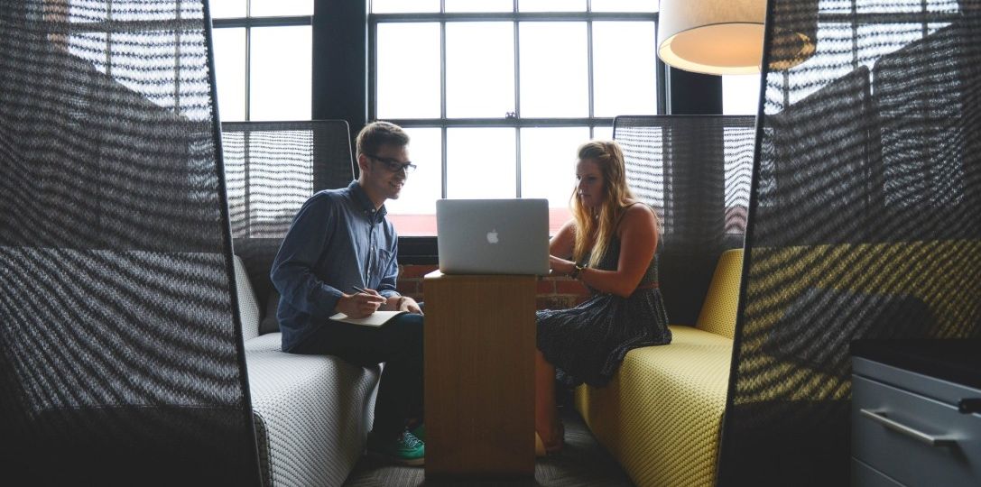 Two people sitting across from each other sharing a laptop and working together