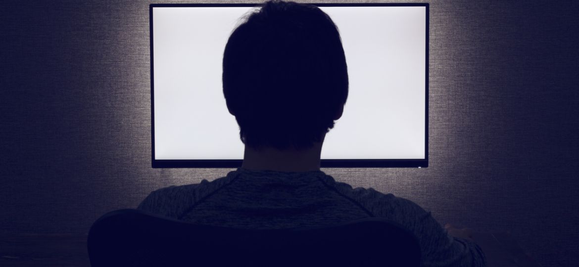 Man sits in front of a blank monitor in dark room